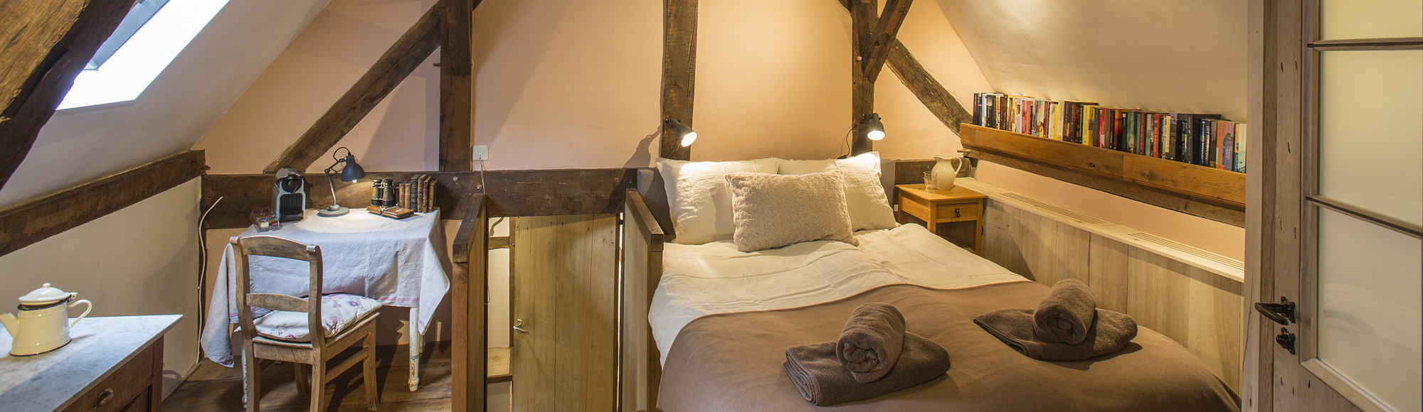 Sfeervolle hotelkamer onder een schuin dak met houten balken.