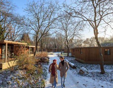 Twee mensen wandelend door de sneeuw langs houten huisjes