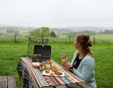 Dame zit aan picknicktafel gevuld met lekkers terwijl ze uitkijkt over het landschap