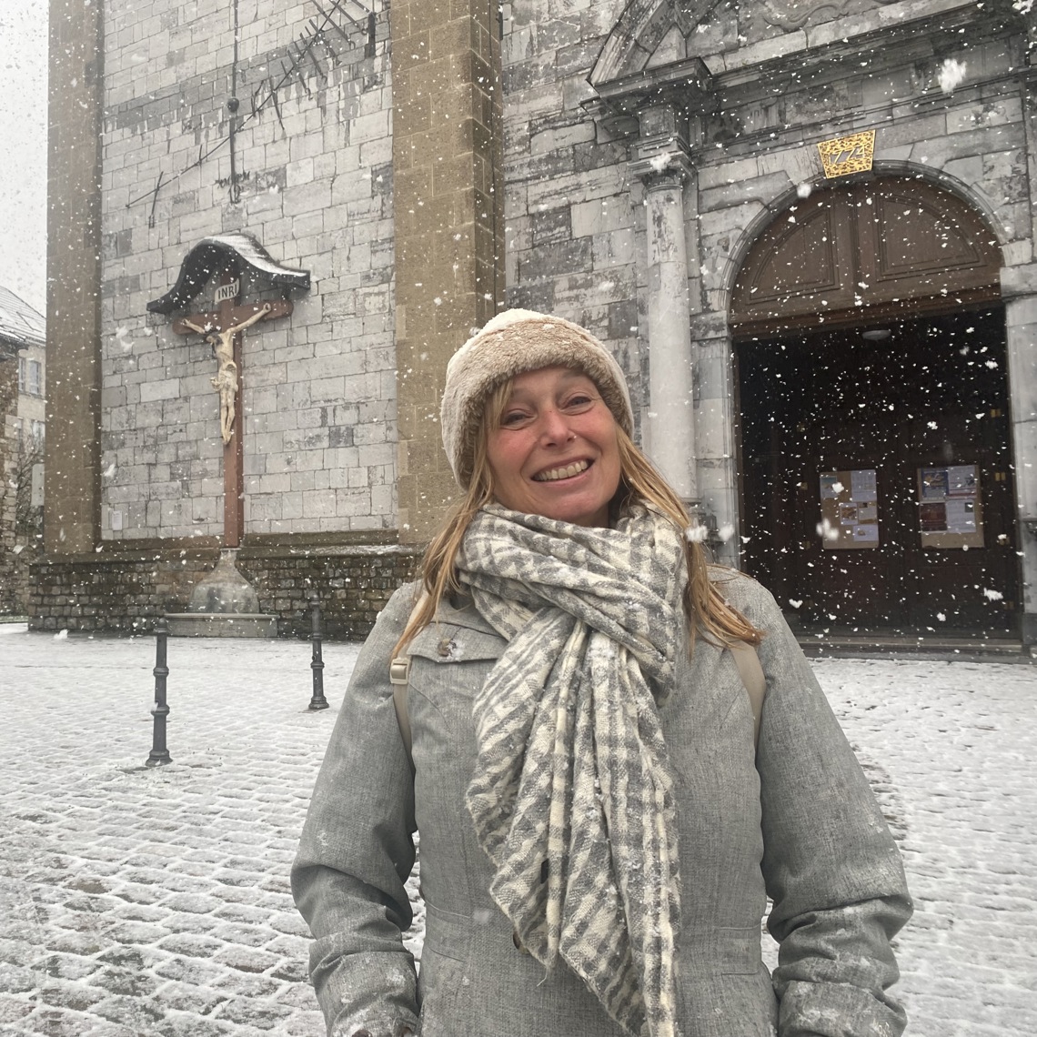 Vrouw met muts en sjaal in de sneeuw voor een kerk.