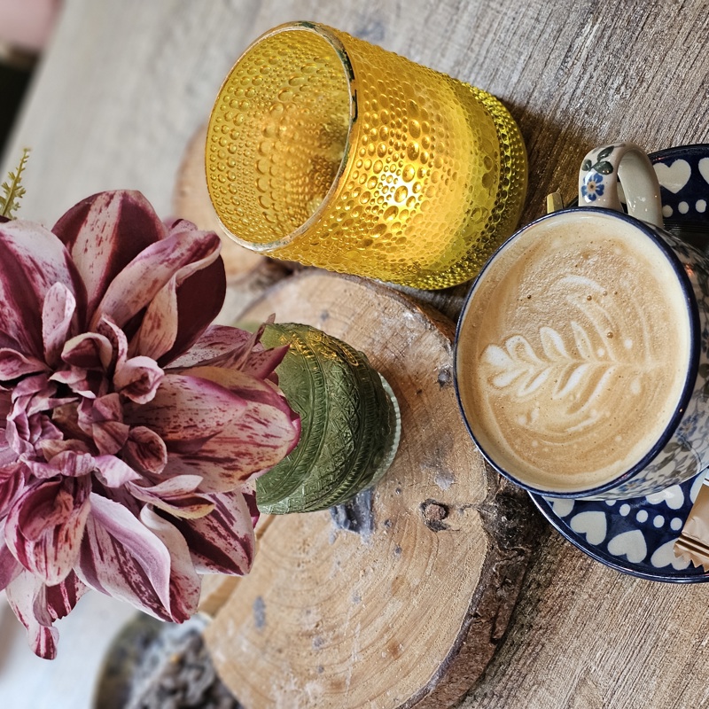 Een mooi geserveerd kopje koffie bij een kleurrijk bloemetje op een houten tafel