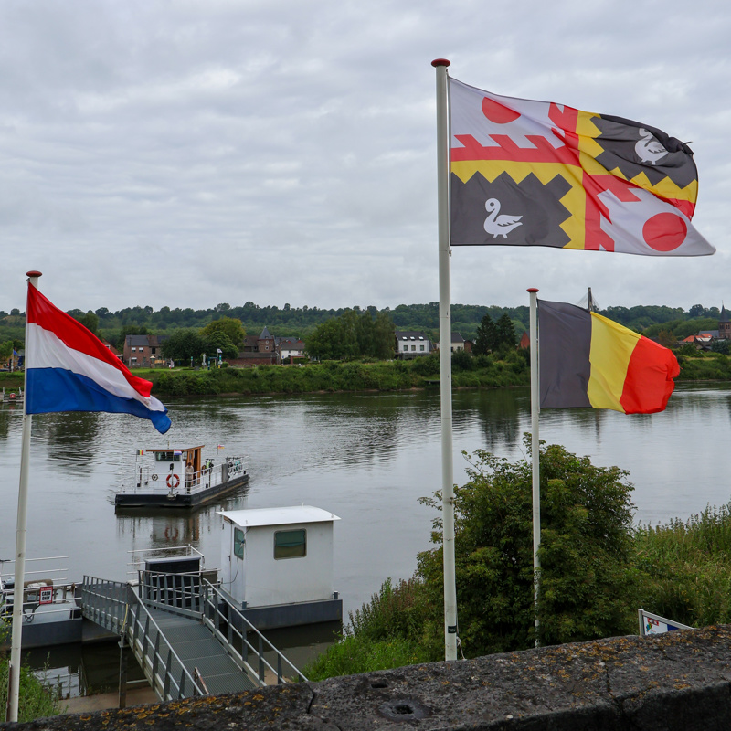 Veerpondje steekt over de Maas in Eijsden met wapperende vlaggen aan de kade. 