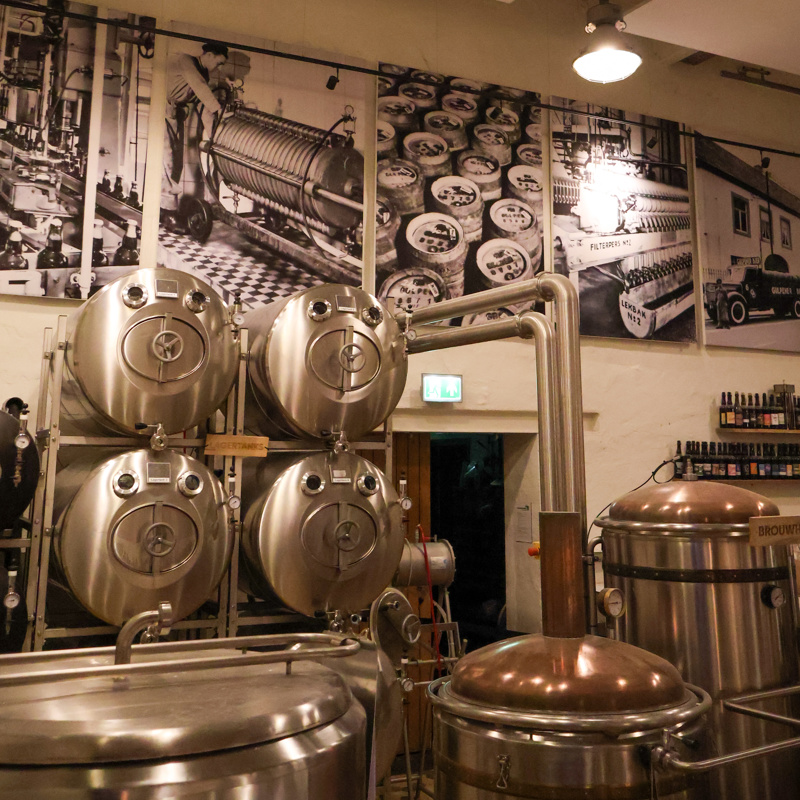 Biervaten in een brouwerij met oude foto's aan de muur. 