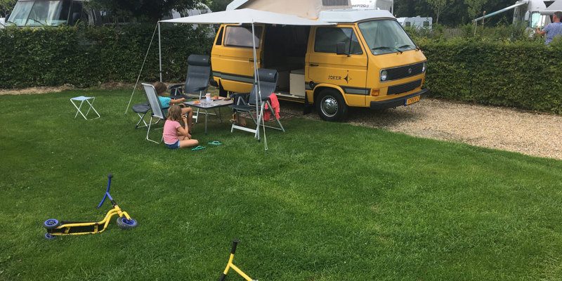 Geel campeerbusje met kinderen en stepjes ervoor. 