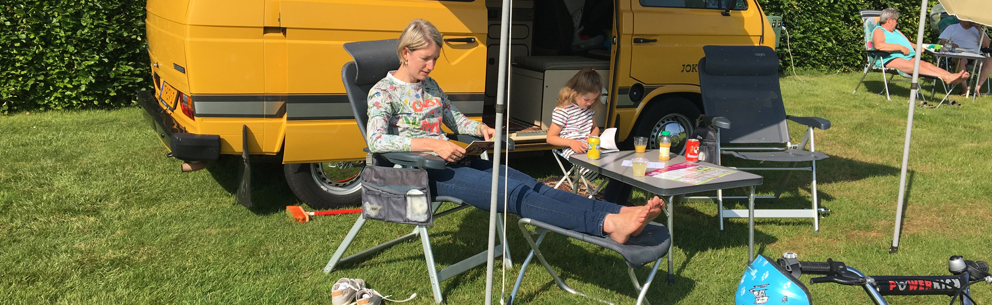 Moeder en dochter zitten in een stoel voor het camperbusje op de camping. 