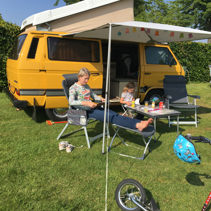 Moeder en dochter zitten in een stoel voor het camperbusje op de camping. 