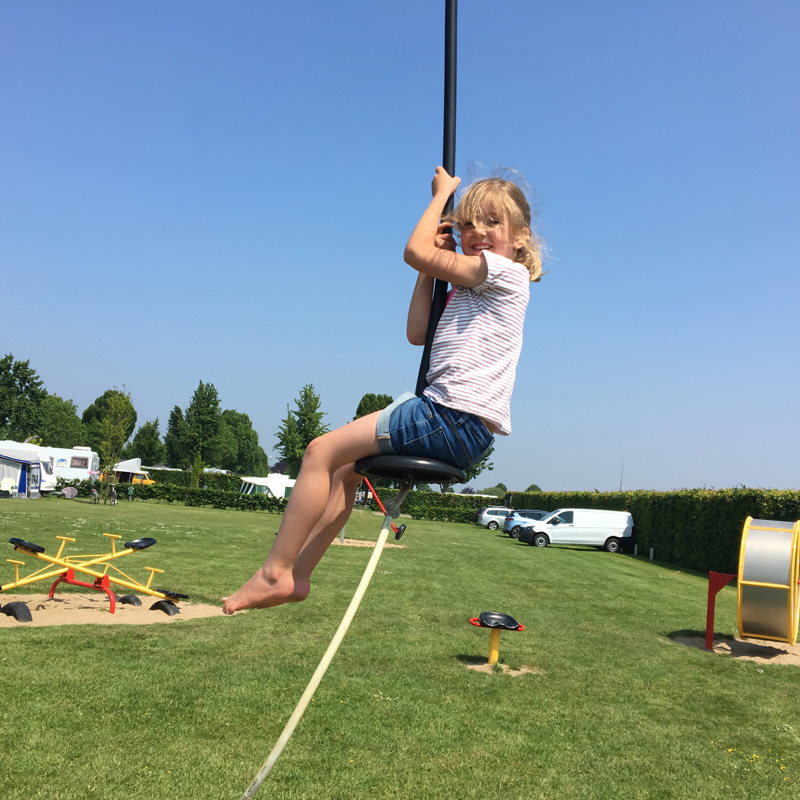 Meisje zit op tokkelbaan in de speeltuin op de camping. 