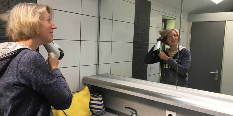 Vrouw is haren aan het fohnen in sanitairgebouw van de camping. 