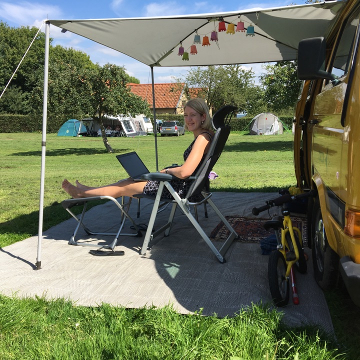 Dame in campingstoel met de benen omhoog is op de laptop aan het werk. 