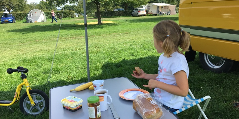 Meisje eet een broodje aan een tafeltje op de camping. 
