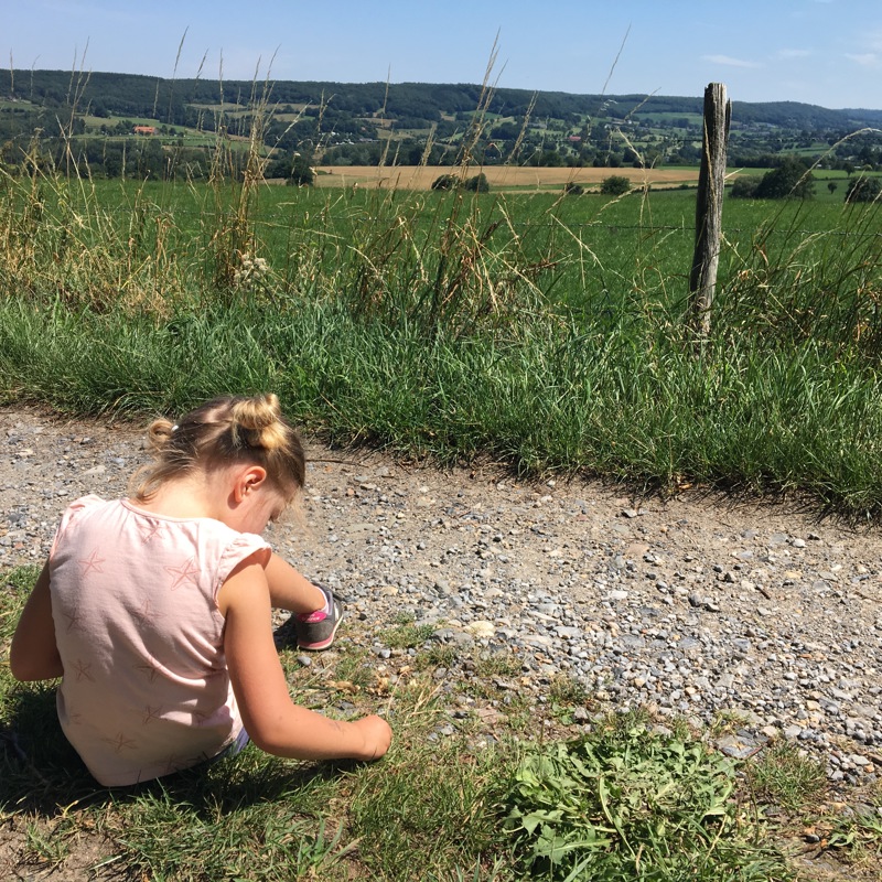 Meisje met blonde staartjes zit op een wandelpad in het Heuvelland. 