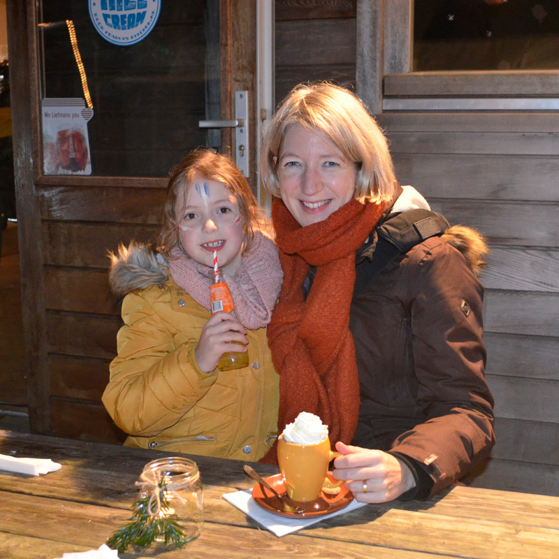 vrouw en meisje met dikke winterjas zitten binnen aan de warme chocomel met slagroom