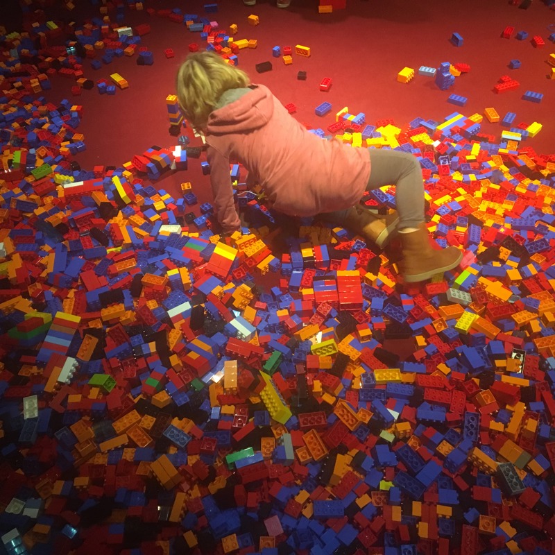 Meisje speelt op een met duplo bezaaide rode vloer