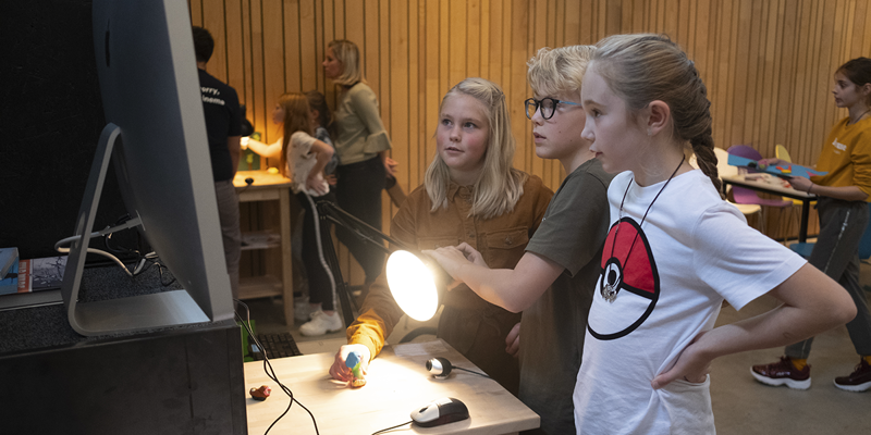 Kinderen schijnen met lamp op poppetje terwijl ze naar beeldscherm kijken