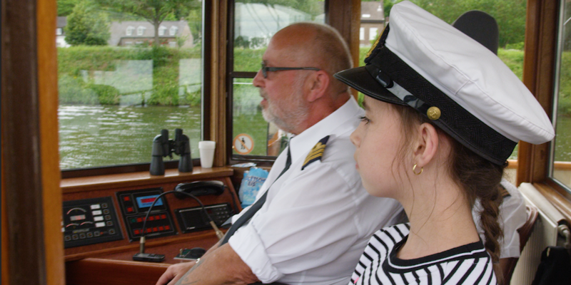 Meisje met kapiteinspet naast de kapitein op een boot kijkende over het water