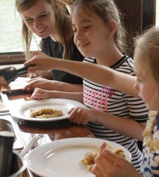 Jonge vrouw en 2 meisjes scheppen eten op op een boot