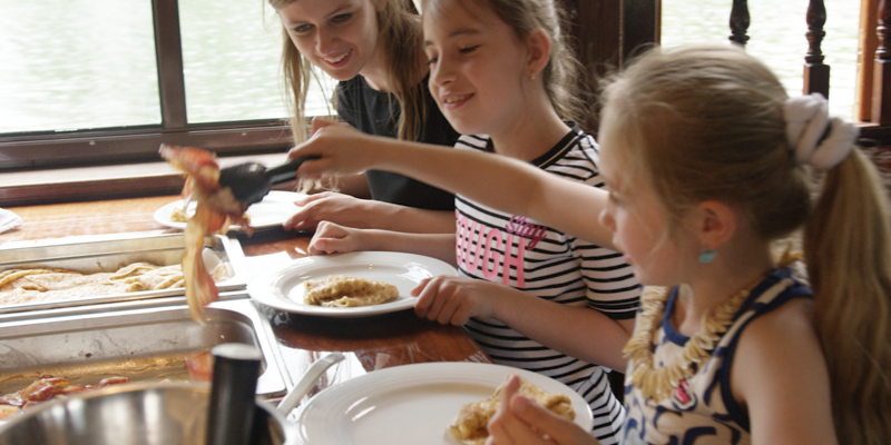 Jonge vrouw en 2 meisjes scheppen eten op op een boot