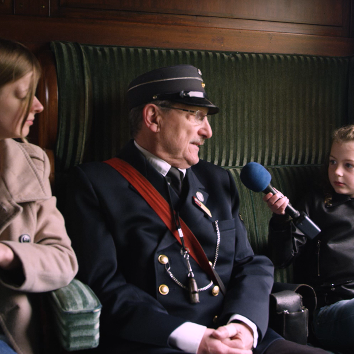 Meisje interviewt conducteur in oud treinstel