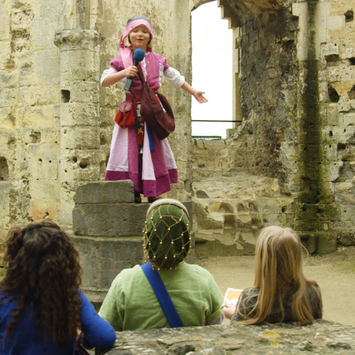 Verkleed meisje met microfoon bovenop oude waterpunt op kasteelruine Valkenburg. Andere kinderen kijken toe