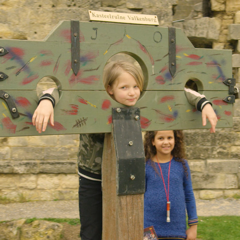 Kind poseert met handen en hoofd in schavot bij kasteelruine Valkenburg