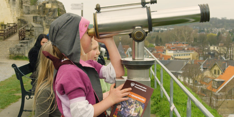 Verkleed kind kijkt door vaste verrekijker bovenop kasteelruine Valkenburg