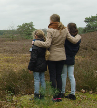 Presentatrice houdt haar handen op de schouders van 2 meisjes wanneer ze uitkijken over de Brunssumerheide