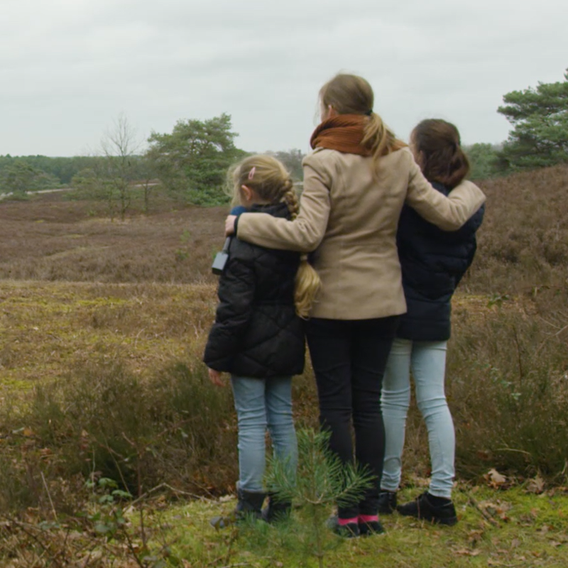 Presentatrice houdt haar handen op de schouders van 2 meisjes wanneer ze uitkijken over de Brunssumerheide