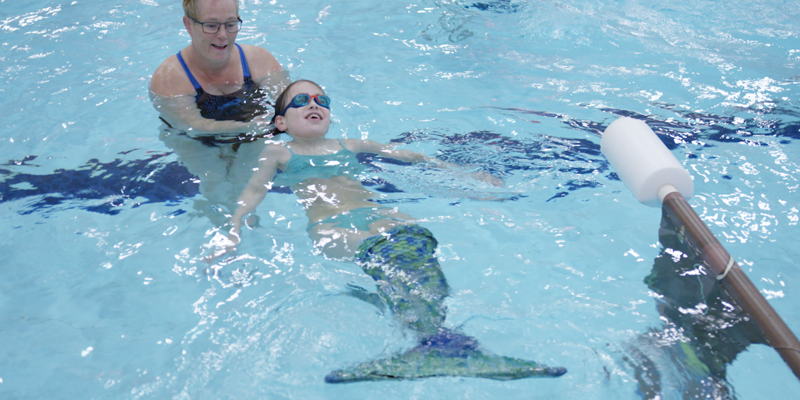 Meisje met zeemeerminstaart drijft op rug in zwembad