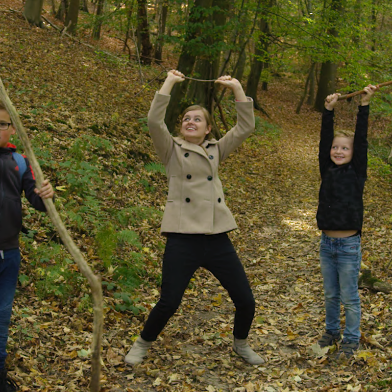 Jonge vrouw en 2 jongens houden ieder een tak boven hun hoofd in het bos