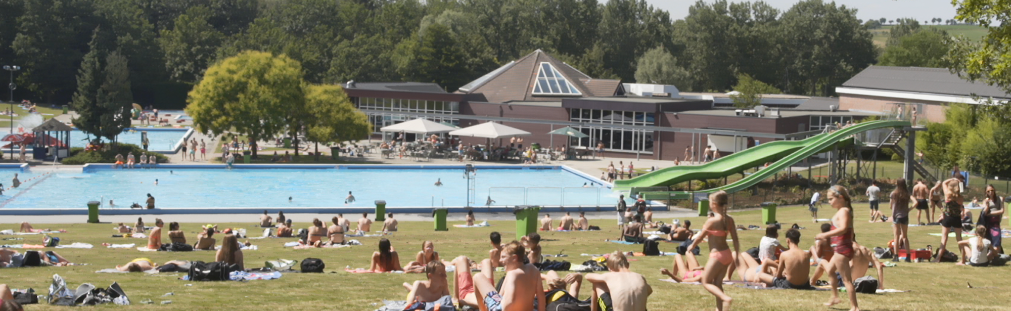 Overzichtsfoto van zonnende mensen in gras bij buitenbad Mosaqua