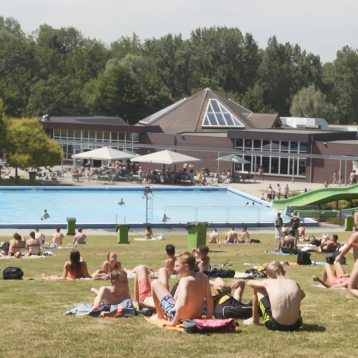 Overzichtsfoto van zonnende mensen in gras bij buitenbad Mosaqua