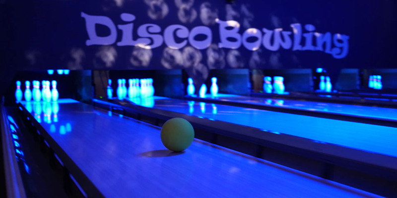Gele bowlingbal rolt over bowlingbaan tijdens discobowling