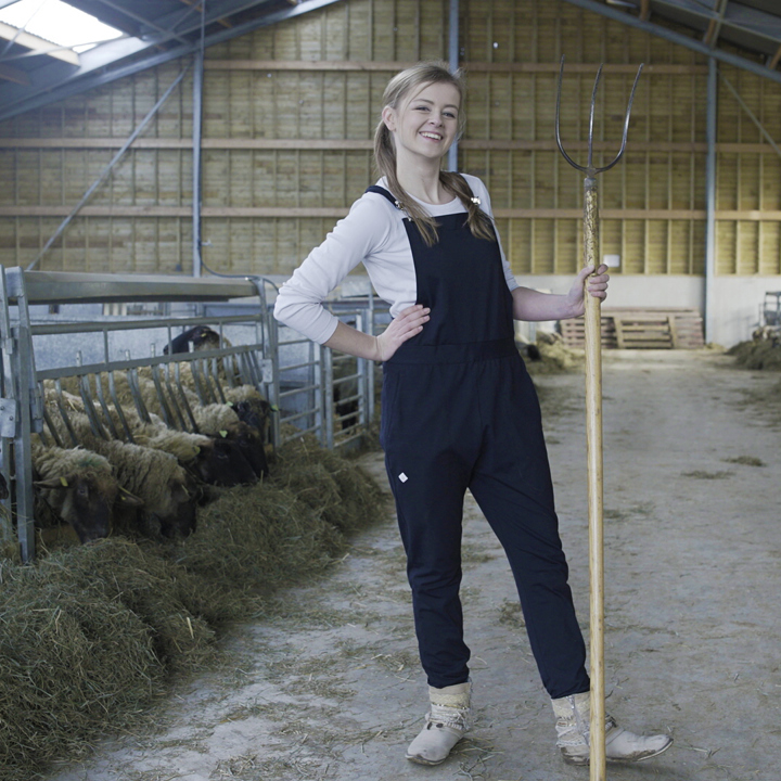 Meisje met zwarte overall en hooivork in schaapskooi