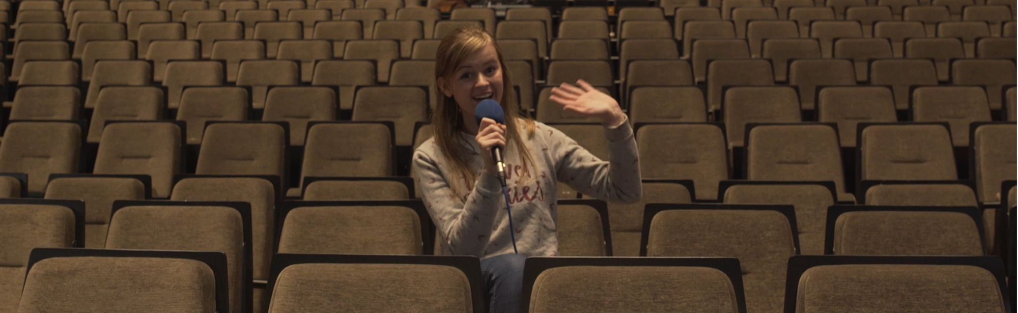 Presentatrice op een stoel in een lege theateropstelling