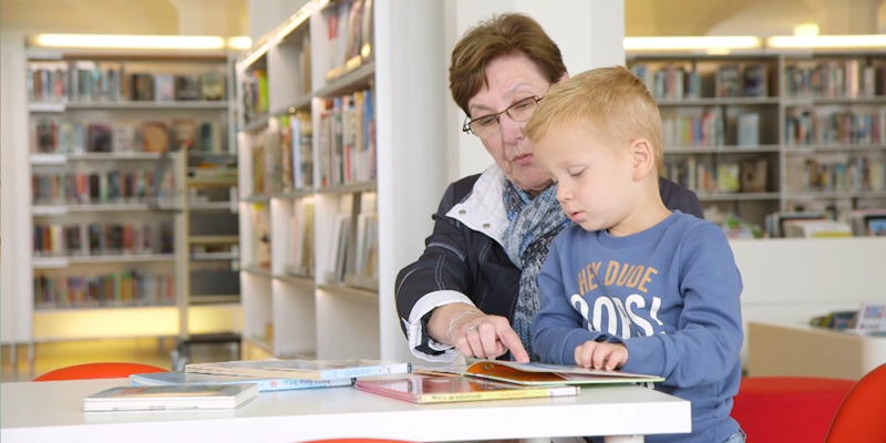 Oudere vrouw met jongetje op schoot wijst in opengeslagen boek