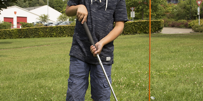 Jongen met golfclub in gras bij oranje vlag