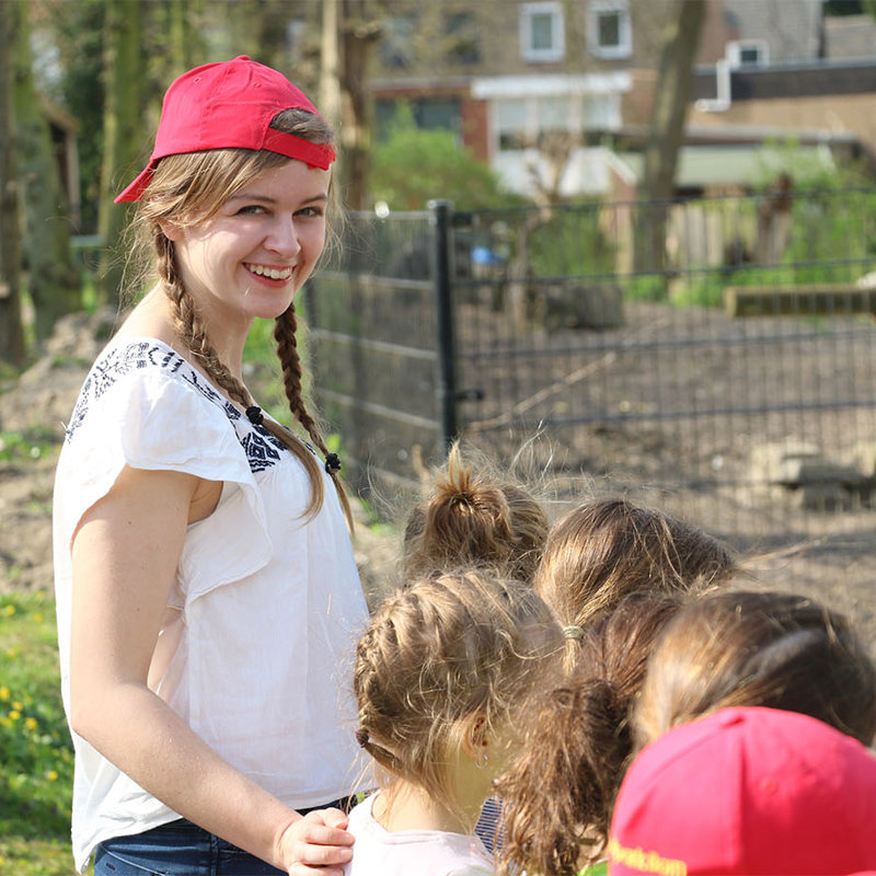 Jonge vrouw met rood petje en groep kinderen kijken naar dieren in dierenverblijf