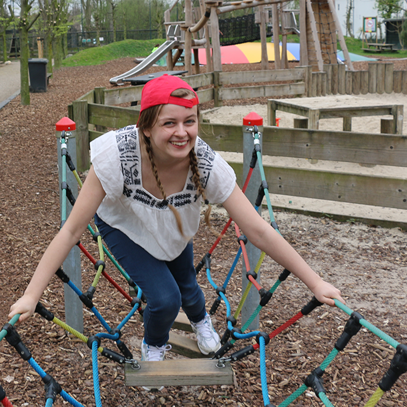 Jonge vrouw met rood petje klimt op klimtoestel in speeltuin