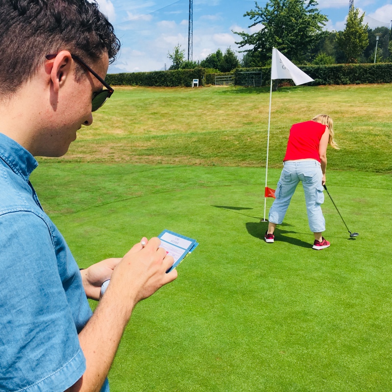 Man houdt score bij, terwijl vrouw probeert het golfballetje naar de vlag te schieten