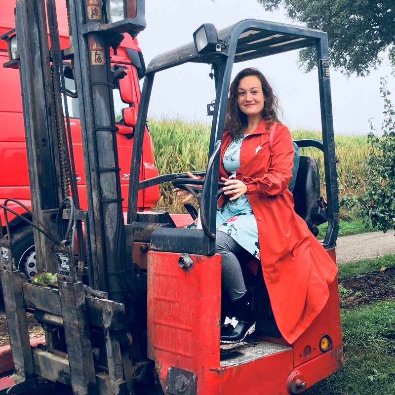 Een vrouw in een rode jas probeert een stukje te rijden in een rode mini heftruck