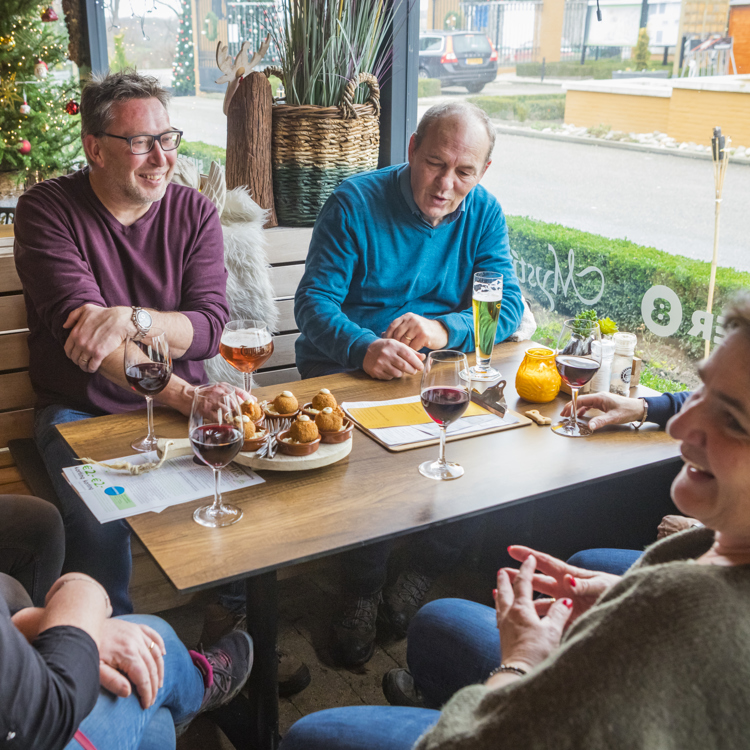 Vriendengroep zit rond een tafel waarop drankjes en fancy bitterballen staan