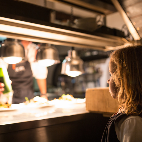 Kind staat in de keuken van een restaurant en bekijkt hoe de koks het eten bereiden