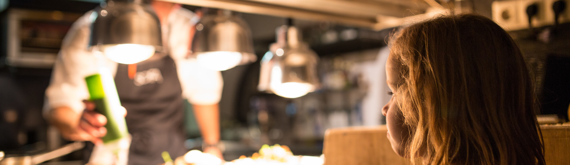 Kind staat in de keuken van een restaurant en bekijkt hoe de koks het eten bereiden