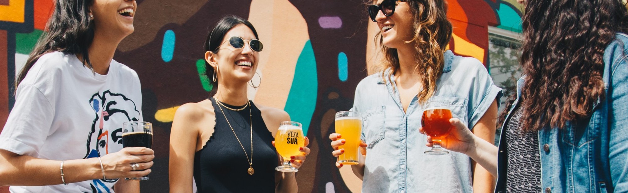 Vier vrouwen genieten van een speciaalbiertje in de zon met zomerse kleding en een graffiti achtergrond