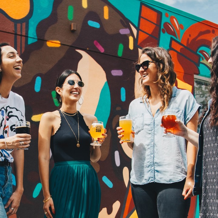 Vier vrouwen genieten van een speciaalbiertje in de zon met zomerse kleding en een graffiti achtergrond