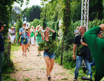 Hopoogstfeesten met de fanfare, een feestvierende dame met hop om haar schouders en een man met een Gulpener biertje