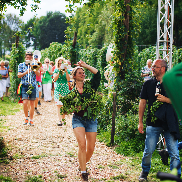 Hopoogstfeesten met de fanfare, een feestvierende dame met hop om haar schouders en een man met een Gulpener biertje