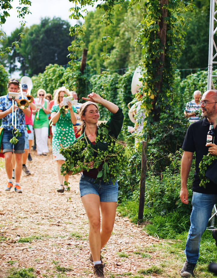 Hopoogstfeesten met de fanfare, een feestvierende dame met hop om haar schouders en een man met een Gulpener biertje