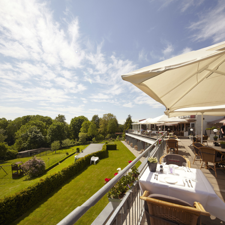 Zonnig terras op eerste verdieping met uitzicht over een mooie tuin met veel groen.