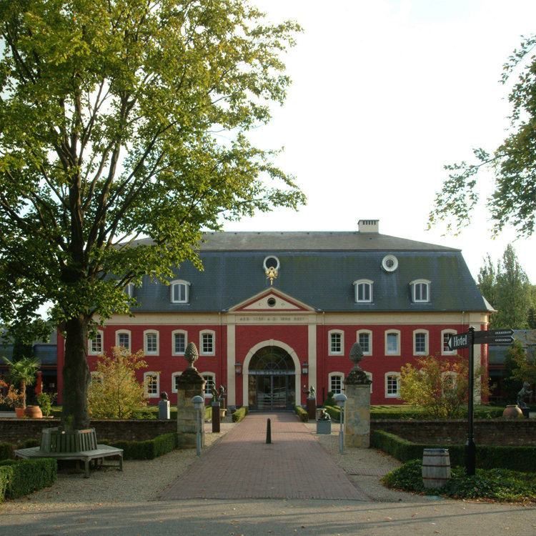 Buitenaanzicht van een roodkleurig chateau en een wandelpad in het midden. 